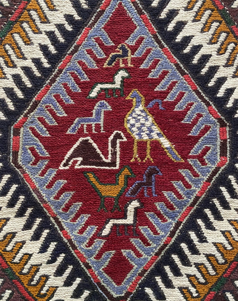 May include: A red, blue, and white patterned rug with a diamond-shaped design featuring stylized birds and animals. The rug has a traditional, folk art style.