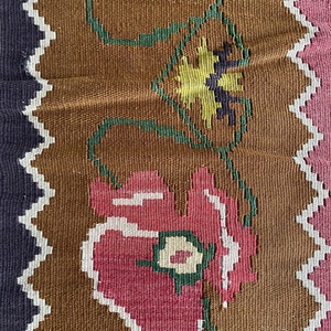 May include: Close-up of a brown woven fabric with a repeating pattern of pink, white, and green flowers. The flowers have a stylized design and are connected by green vines.