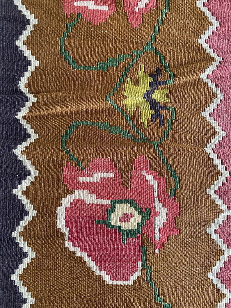May include: Close-up of a brown woven fabric with a repeating pattern of pink, white, and green flowers. The flowers have a stylized design and are connected by green vines.