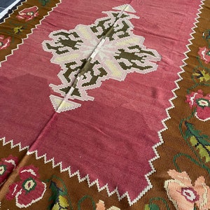 May include: A traditional style rug with a pink center and a brown border. The border features a floral pattern with pink, white, and green flowers.