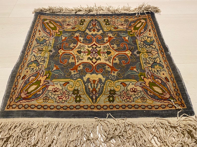 May include: A vintage rug with a blue background and intricate floral patterns in shades of brown, green, and cream. The rug has a fringe border.