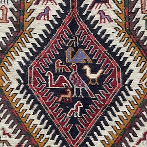 May include: A traditional rug with a geometric pattern in shades of red, white, black, and brown. The center of the rug features a diamond shape with stylized animal figures.