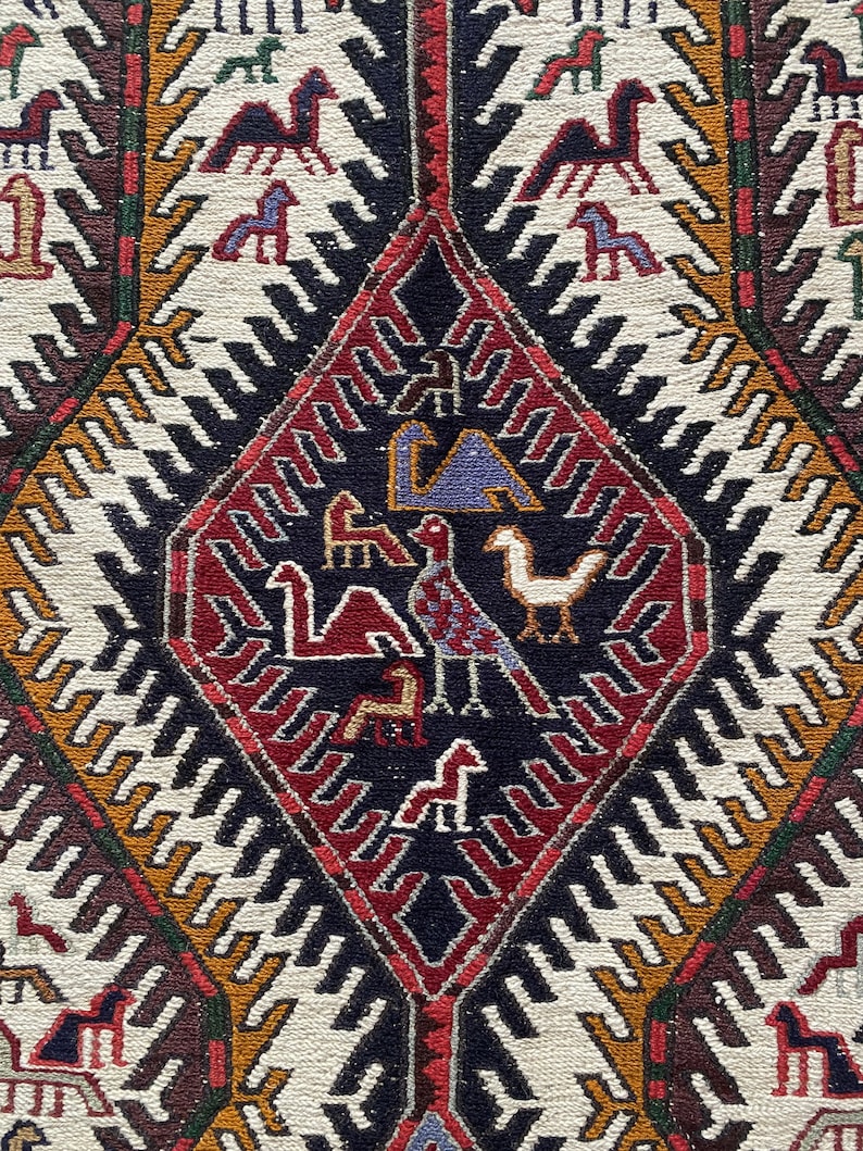 May include: A traditional rug with a geometric pattern in shades of red, white, black, and brown. The center of the rug features a diamond shape with stylized animal figures.