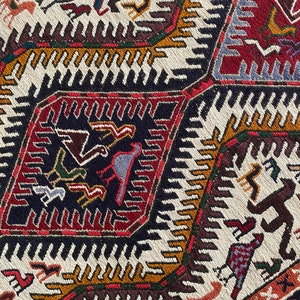 May include: Close-up of a colorful woven rug with geometric patterns and stylized animal figures. The rug features a white background with black, red, brown, blue, and yellow accents.