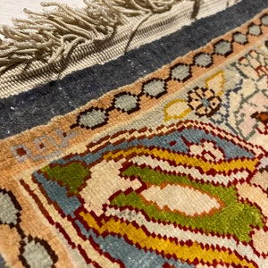 May include: Close-up of a colorful rug with a fringe border. The rug features a geometric pattern with shades of blue, green, red, and yellow.