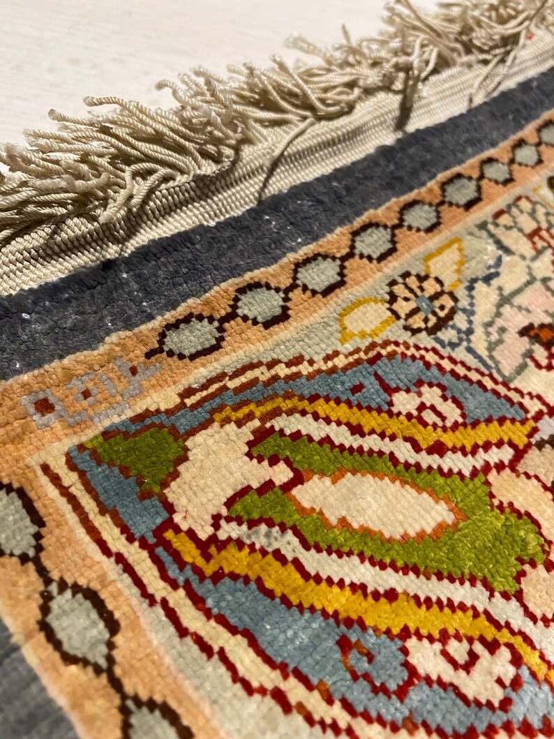 May include: Close-up of a colorful rug with a fringe border. The rug features a geometric pattern with shades of blue, green, red, and yellow.