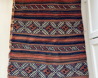 May include: A rectangular rug with a geometric pattern. The rug features alternating stripes of dark blue and reddish-brown, with diamond-shaped patterns in the center. The edges have a tan fringe.