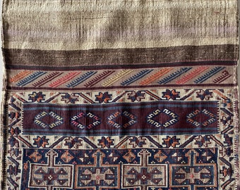 May include: A vintage woven rug with intricate geometric patterns in shades of brown, red, blue, and white. The rug has a fringed edge and a worn, distressed look.