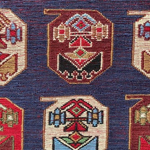 Op de afbeelding: Een close-up van een blauw tapijt met een herhalend patroon van kleurrijke geometrische vormen. Het tapijt heeft een traditioneel ontwerp met ingewikkelde details.