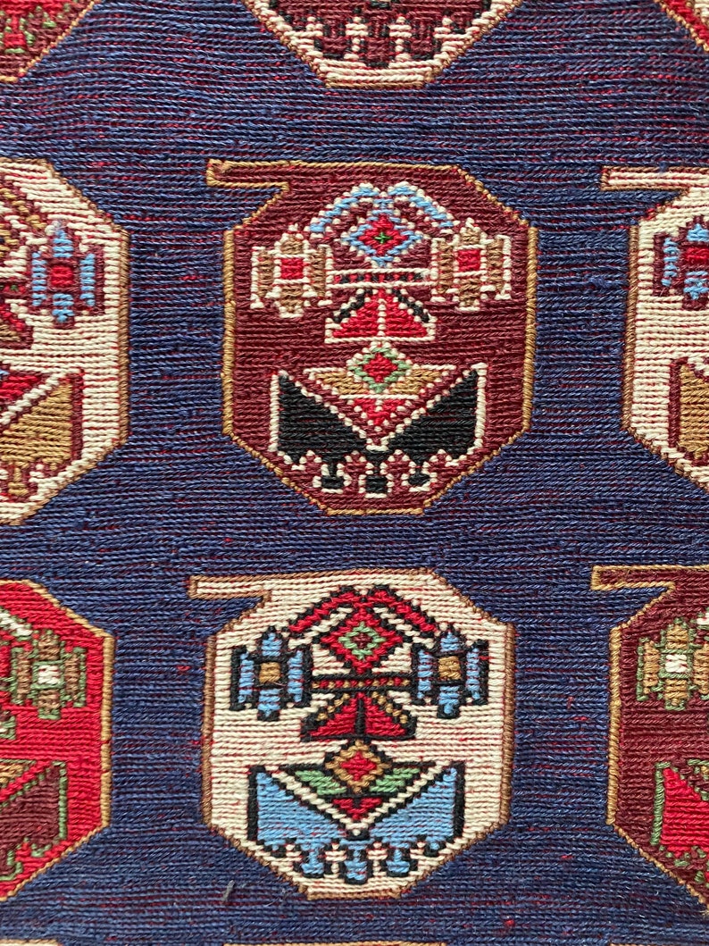 Op de afbeelding: Een close-up van een blauw tapijt met een herhalend patroon van kleurrijke geometrische vormen. Het tapijt heeft een traditioneel ontwerp met ingewikkelde details.