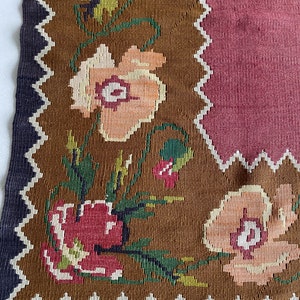 May include: A brown and pink woven rug with a floral pattern. The rug has a fringe border and a geometric design in the center.