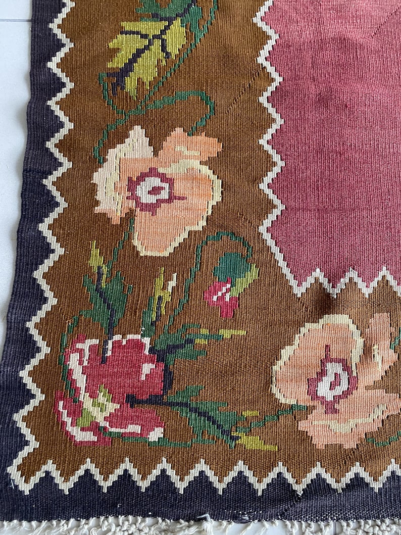 May include: A brown and pink woven rug with a floral pattern. The rug has a fringe border and a geometric design in the center.