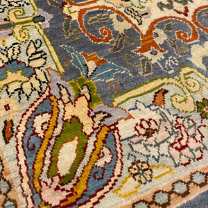 May include: Close-up of a detailed rug with a blue background and intricate patterns in shades of red, yellow, green, and white.