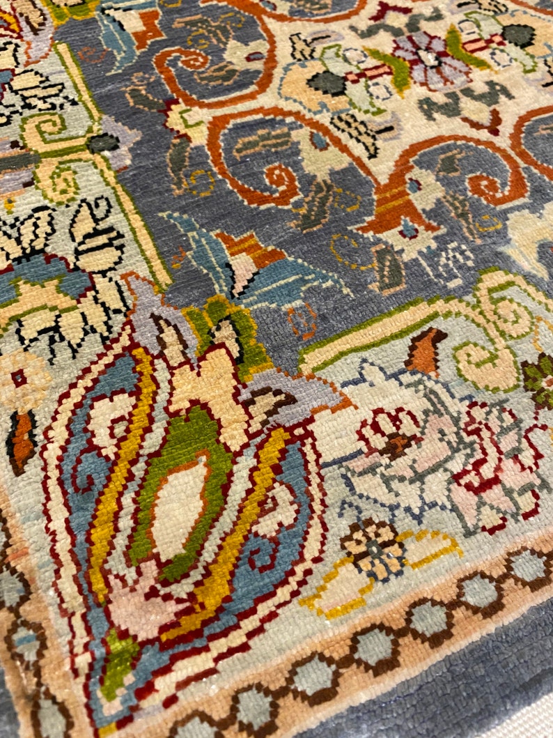 May include: Close-up of a detailed rug with a blue background and intricate patterns in shades of red, yellow, green, and white.