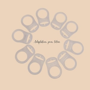 Peut inclure: Plusieurs adaptateurs de sucette en plastique transparent disposés en cercle sur un fond pêche clair. Le texte "Adaptateur pour tétine" est écrit en script.