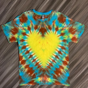 May include: A tie-dye t-shirt with a yellow heart design in the center. The shirt is a blend of blue, green, and brown colors.