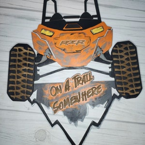 May include: Orange and black wooden cutout of a side-by-side off-road vehicle with the text "ON A TRAIL SOMEWHERE" on the bottom.