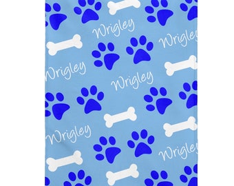 May include: Blue and white personalized dog blanket with paw prints and bone designs. The name "Wrigley" is repeated throughout the blanket.