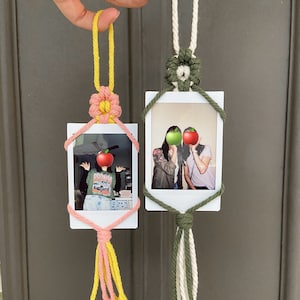 May include: Two polaroid photo frames with macrame string accents. The frames are hanging from a string and have a photo of two people in each. The macrame string is in pink, yellow, white, and green.