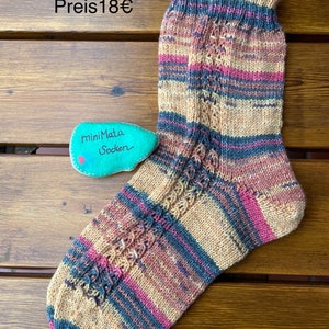 Könnte beinhalten: Ein Paar handgestrickte Socken in einem gestreiften Muster aus Beige, Rosa und Blau. Die Socken haben ein Zopfmuster und sind in Größe 34/35. Der Text "Größe 34/35 Preis 18€" ist im Bild sichtbar.
