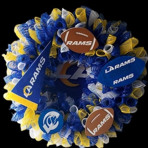 May include: A decorative wreath in blue, yellow, and white mesh, featuring football-shaped ornaments and a pennant, all bearing the "RAMS" logo. The wreath has a black background and the text "C&M Wreaths LLC".