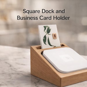 May include: Wooden square dock and business card holder. The holder has a slot for a business card with a gold accent and a white square device. The text "Square Dock and Business Card Holder" is at the top.