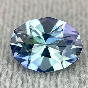 May include: A faceted oval-shaped gemstone with a blue-green hue. The gem has a star-like pattern in the center.