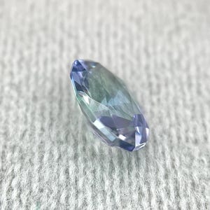 K&ouml;nnte beinhalten: Ein facettierter ovaler Edelstein mit einem blauen und gr&uuml;nen Farbverlauf. Der Edelstein ist vor einem wei&szlig;en Hintergrund platziert.