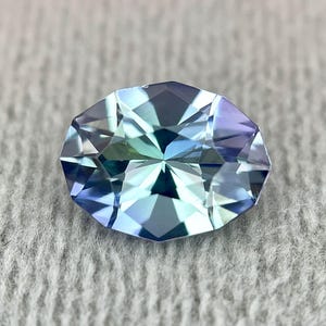 K&ouml;nnte beinhalten: Ein facettierter ovaler Edelstein in blaugr&uuml;ner Farbe. Der Edelstein hat einen hohen Glanz und ist vor einem wei&szlig;en Hintergrund platziert.