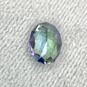 K&ouml;nnte beinhalten: Ein facettierter Edelstein mit einem Farbverlauf von Blau, Gr&uuml;n und Lila. Der Edelstein ist in runder Form geschliffen und hat einen hohen Glanz.