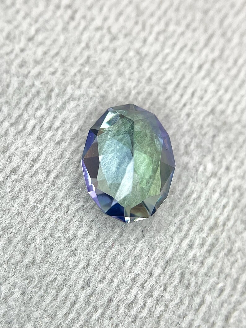 K&ouml;nnte beinhalten: Ein facettierter Edelstein mit einem Farbverlauf von Blau, Gr&uuml;n und Lila. Der Edelstein ist in runder Form geschliffen und hat einen hohen Glanz.