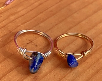 May include: Two wire wrapped rings with blue lapis lazuli stones. The ring on the left has a silver wire and the ring on the right has a gold wire.