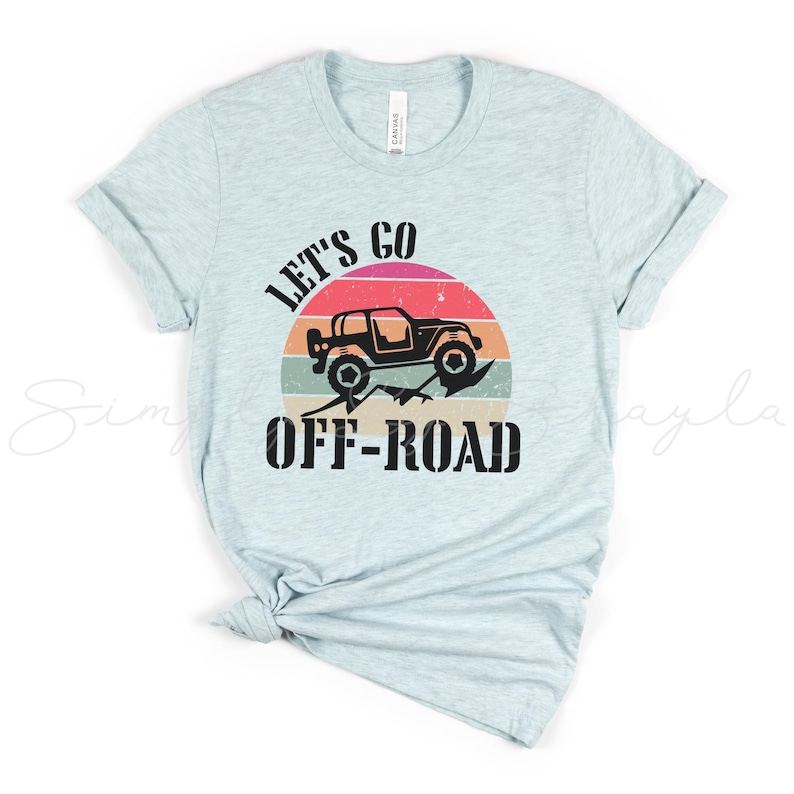 May include: A light blue t-shirt with the text "Let's Go Off-Road" in black. A black silhouette of a jeep driving over a mountain range is in a sunset-colored circle behind the text.