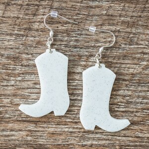 May include: A pair of white glitter cowboy boot earrings with silver hooks.