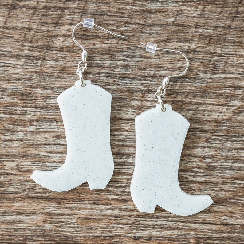 May include: A pair of white glitter cowboy boot earrings with silver hooks.