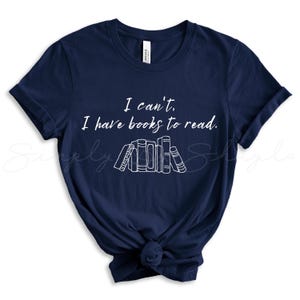 May include: Navy blue t-shirt with white text that reads "I can't. I have books to read." and a graphic of a stack of books.