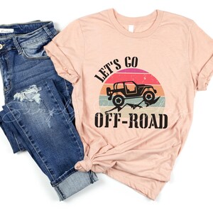 May include: A peach-colored t-shirt with a black graphic of a jeep driving off-road with a sunset behind it. The text "Let's Go Off-Road" is printed below the jeep.