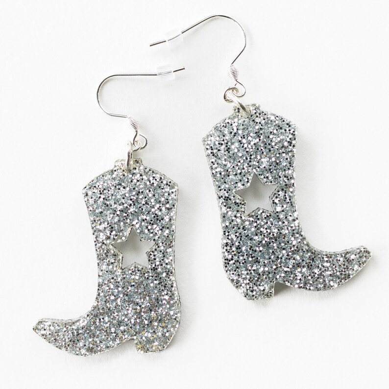 May include: Silver glitter cowboy boot earrings with a star cut-out. The earrings have silver hooks.