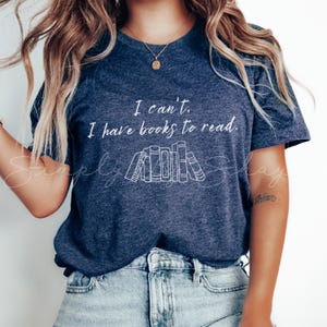 May include: A navy blue t-shirt with the text "I can't, I have books to read." in white. A graphic of a stack of books is below the text.