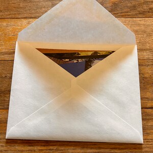 May include: A white envelope with a flap open, revealing a photograph inside. The photograph is partially visible and appears to be a landscape scene.