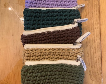 Peut inclure: Cinq pochettes à fermeture éclair en crochet empilées les unes sur les autres. Les pochettes sont de différentes couleurs, notamment violet, vert, marron, beige et vert foncé.