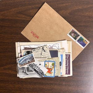 Könnte beinhalten: Ein brauner Papierumschlag mit einem roten Stempel, auf dem "HANDLE WITH CARE DO NOT BEND THANK YOU" steht. Der Umschlag ist gefüllt mit alten Postkarten, Briefmarken und anderen Ephemera.