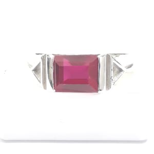May include: A silver ring with a rectangular, red gemstone set in the center. The ring has two triangular accents on either side of the gemstone.