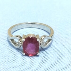 May include: A silver ring with a pink oval gemstone and two smaller clear gemstones on either side.