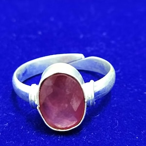 May include: A silver ring with a pink oval gemstone set in the center. The ring is on a blue background.
