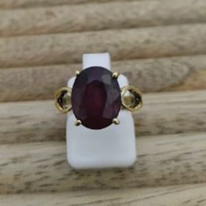 May include: A gold ring with a large oval-shaped purple gemstone and two smaller round gemstones on the sides.