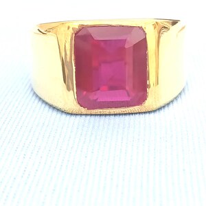 May include: A gold ring with a large, square-shaped, red ruby gemstone.