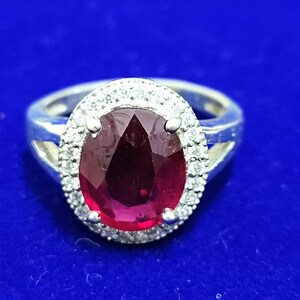 May include: A silver ring with a large, oval-shaped ruby surrounded by smaller diamonds.