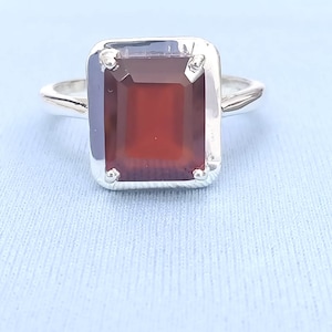 May include: A silver ring with a red gemstone set in a square bezel.