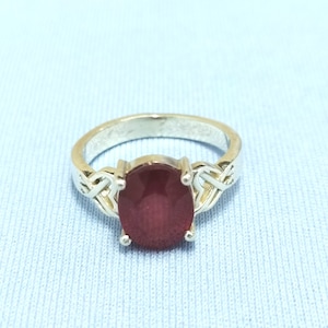 May include: A silver ring with a red oval gemstone set in a Celtic knot design.